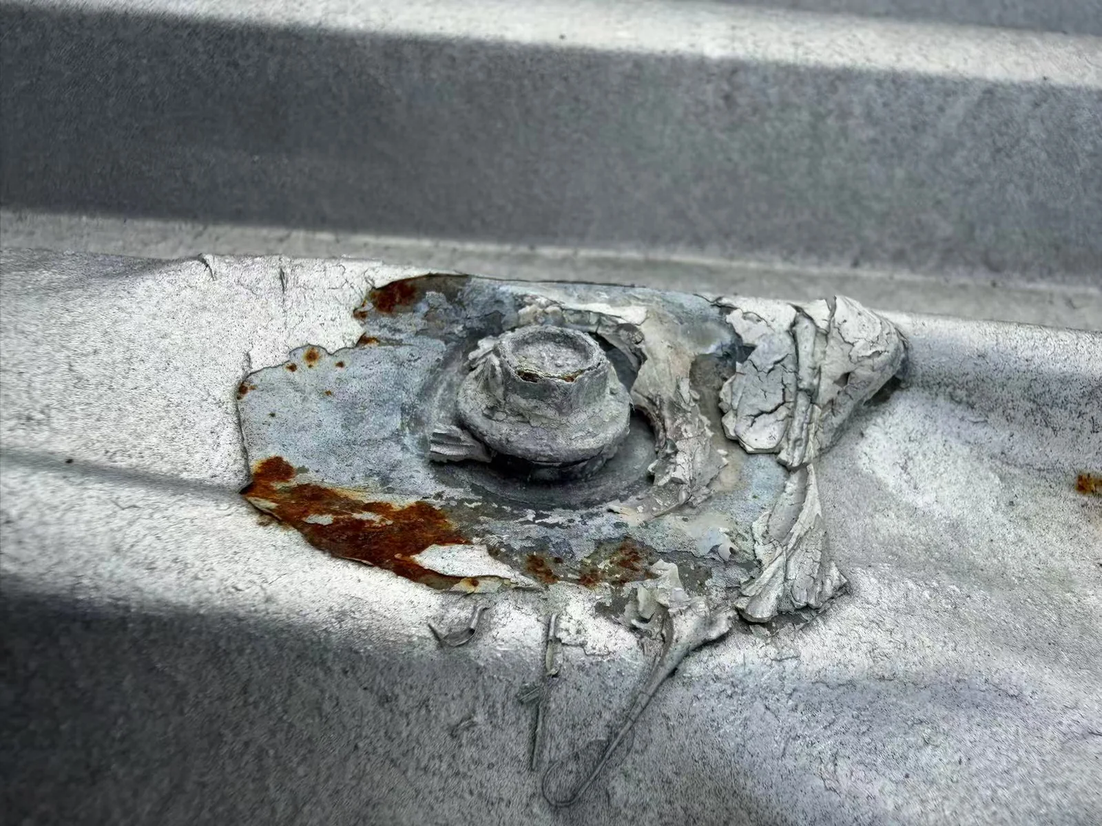 Weathered sealant and corrosion around a metal roof fastener